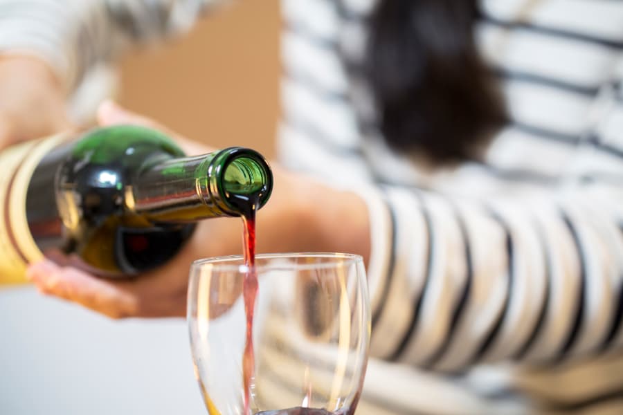 Person in striped shirt pouring red wine into glass