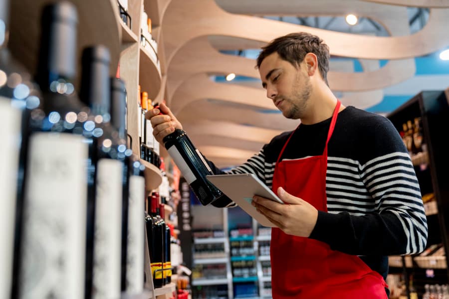 Employee in apron examining wine for retail order online