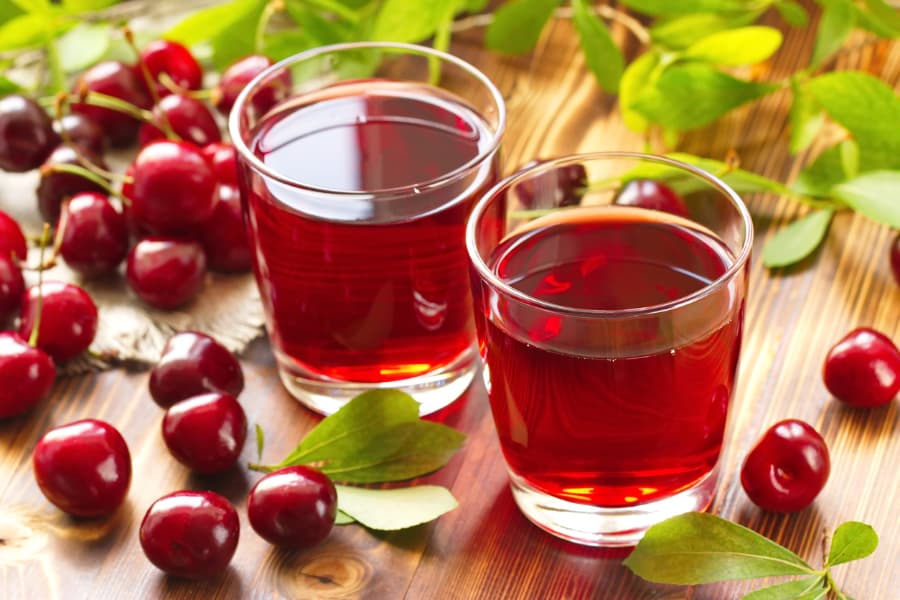 Two glasses of cherry juice surrounded by fresh cherries