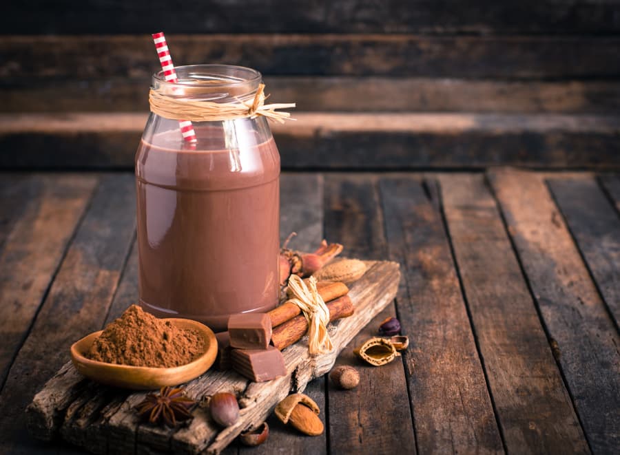 Chocolate milk in jar with bowl of cocoa and cinnamon sticks