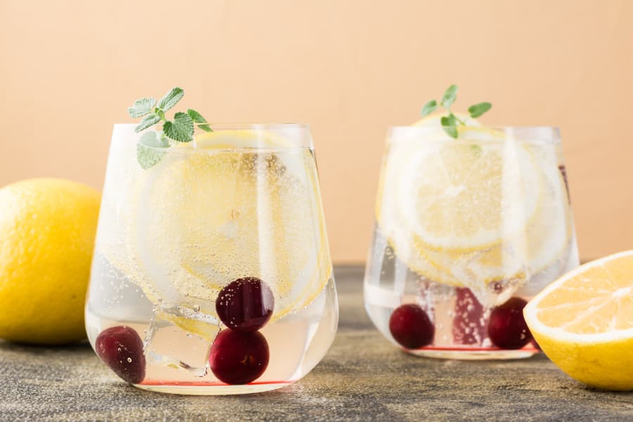 Glasses of hard seltzer with lemons and cherries on table  