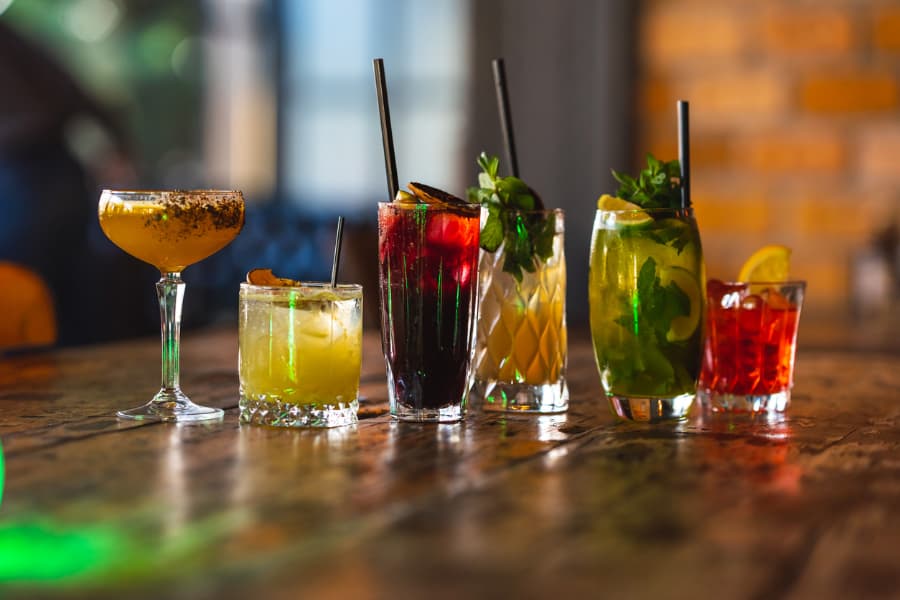 Closeup of five cocktails with garnishes being held in celebratory toast