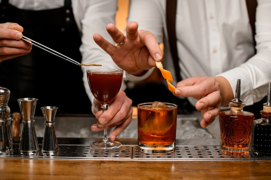 Male bartenders using a channel knife to create garnishes out of an orange peel