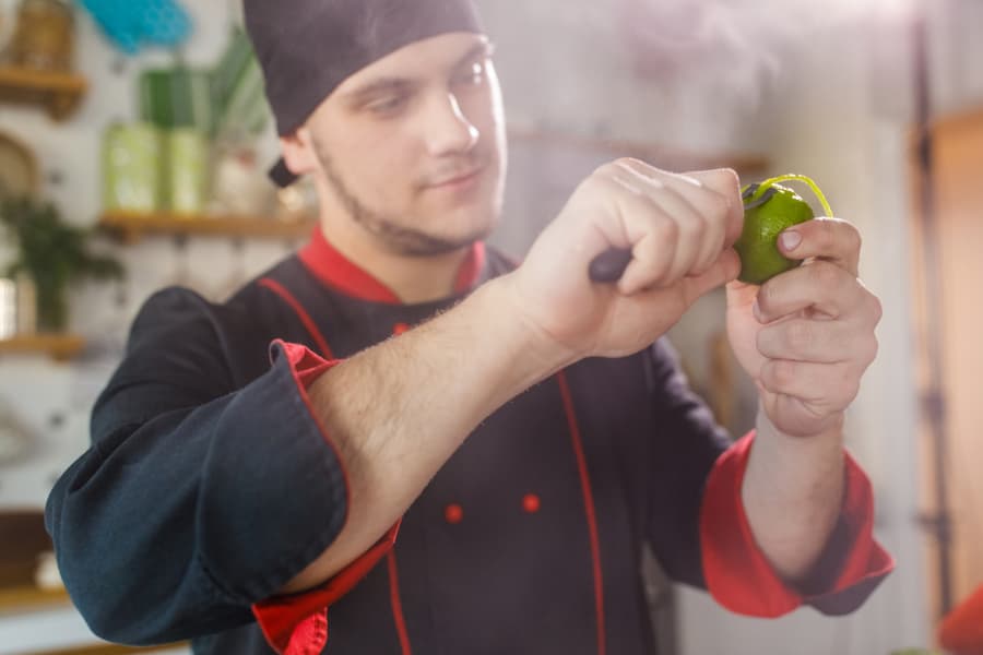 Male chef using a channel knife to peel a lime