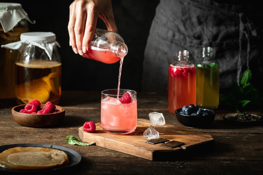 Woman pouring hard kombucha into glass garnished with raspberry