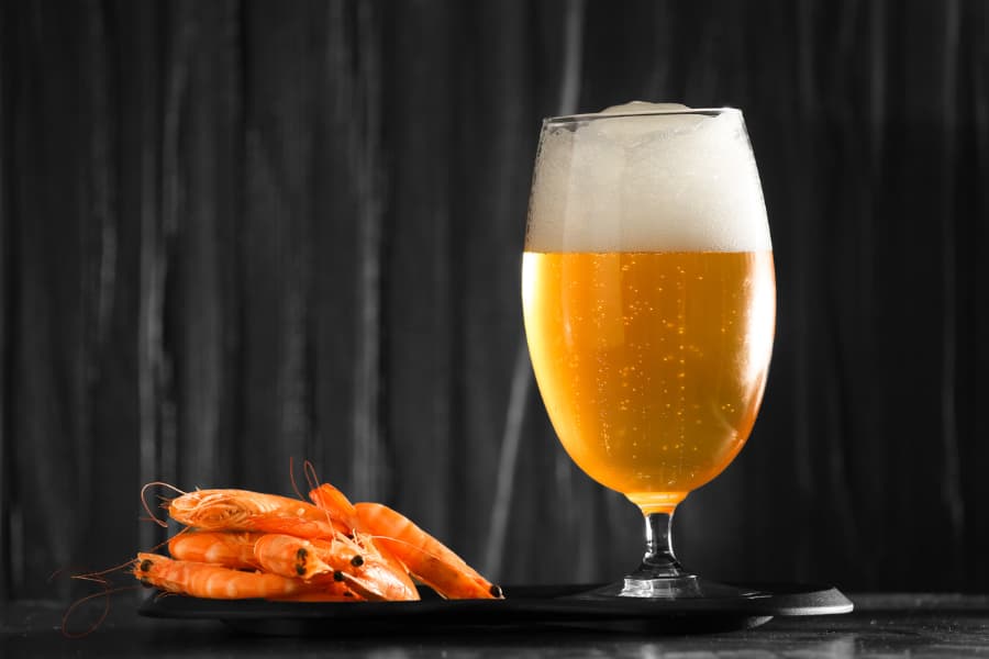 Glass of beer placed next to plate of shrimp 
