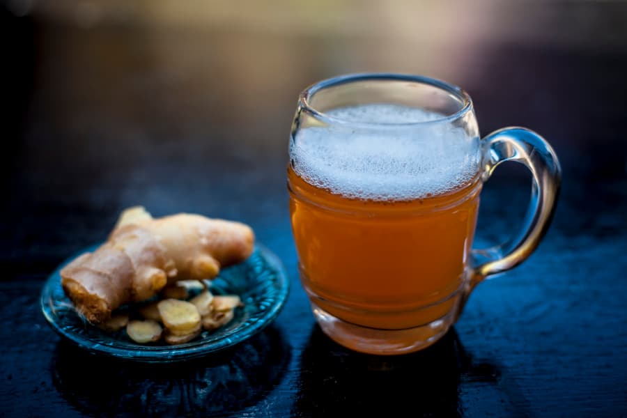 Ginger beer poured in glass sitting on top of bar with ginger root next to it