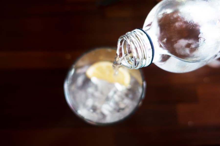 Pouring club soda out of bottle into glass over ice