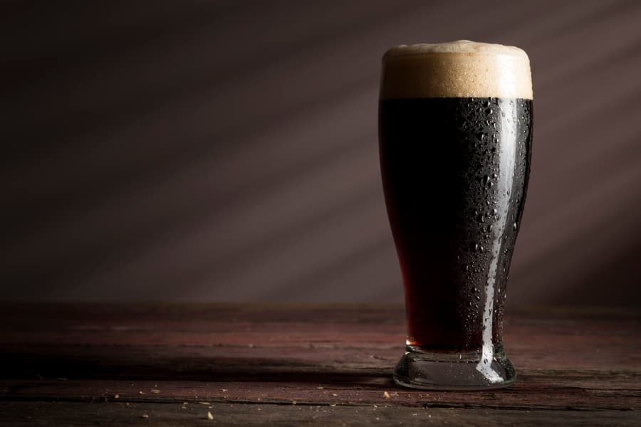 Glass of dark lager beer with foam on table