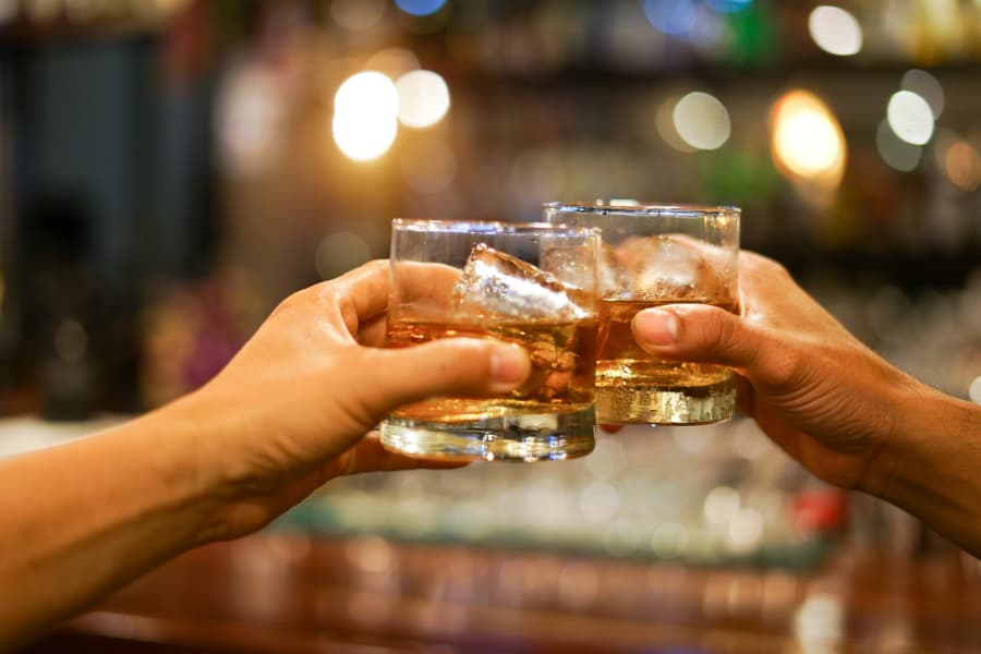 Two partygoers clink glasses of whiskey together